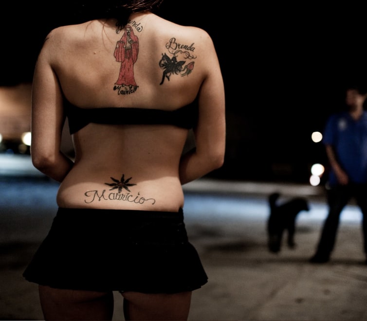  the back of a tattooed feminine figure in a halter top and mini skirt standing outside
